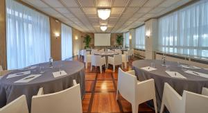 a banquet room with tables and white chairs and windows at Hotel Astoria in Biella
