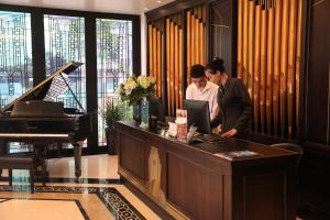 two men standing at a reception desk with a piano at Hotel du Monde Art in Hanoi