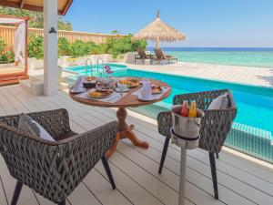a patio with a table and chairs next to a pool at Malahini Kuda Bandos Resort in North Male Atoll