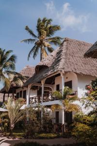 a building with a thatched roof and a palm tree at Blue Oyster Hotel in Jambiani