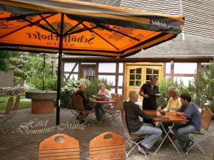 un grupo de personas sentadas en mesas bajo un paraguas en Hotel Demminer Mühle, en Demmin
