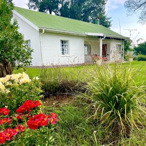 an old white house with flowers in the yard at Bellevue Berg Cottage in Bergville