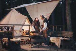 a man and woman cooking food on a grill in front of a tent at Vristulvens Glamping in Mariestad