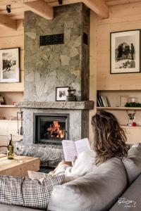 a woman sitting on a couch reading a book in front of a fireplace at Luxury Chalet Villa Gorsky Hanco & Janso in Poronin