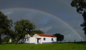 Ein Regenbogen über einem weißen Haus auf einem Feld in der Unterkunft Apartamento das Bolotas. in Lavre