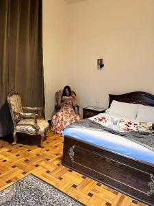Una donna seduta su una sedia in una camera da letto di Hyde Park House Hotel ad Alessandria d'Egitto