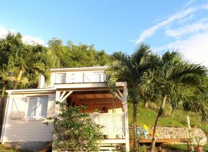 a white house with palm trees in front of it at Caraïbes Cottages Le Jasmin vue mer a 500m de la plage in Deshaies