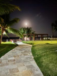 un vialetto in un parco con palme di notte di PORTO CAYMAN RESIDENCE - BEIRA MAR - próximo a Igreja de São Pedro de Padre Arlindo - a Tamandaré