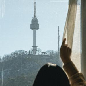 uma pessoa está olhando para fora de uma janela para uma torre em Dears Myeongdong em Seul