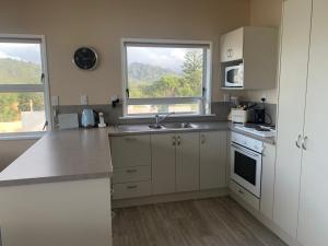 a kitchen with white cabinets and a sink and two windows at Hosts on the Coast Paradise on Pipi in Whangamata