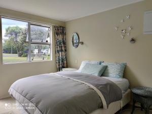 a bedroom with a large bed and a window at Hosts on the Coast Paradise on Pipi in Whangamata