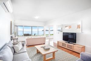 a living room with a couch and a tv at Beached Inn Spacious beach front house in Salamander Bay