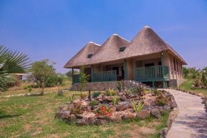 una casa con tetto di paglia e una aiuola floreale di Tilenga Safari Lodge a Arua