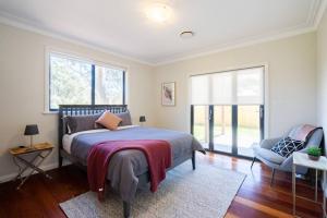 a bedroom with a bed and a chair and windows at Alleura House Serene Bushland 4BR Families Groups in Leura