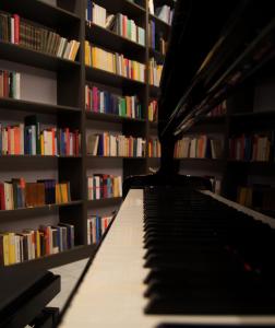 un piano dans une bibliothèque avec des livres dans l'établissement O Mikros Kosmos Hotel Resort - Adults Only, à Sívas