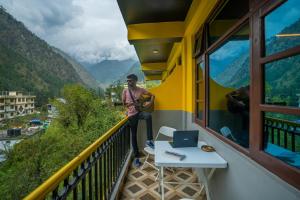un hombre parado en un balcón con vistas a las montañas en The Hosteller Kasol en Kasol