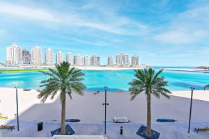 Retaj Baywalk Residence في الدوحة: اطلالة على شاطئ فيه نخل ومباني