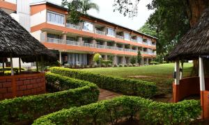 Kakamega的住宿－Golf Hotel Kakamega，一座橙色的建筑,前面有灌木丛