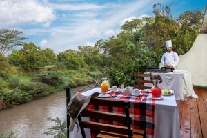 a man standing on a deck with a table next to a river at PrideInn Mara Camp & Cottages in Talek +160 photos
