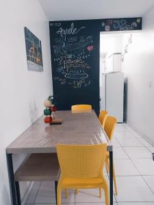 a dining room table with yellow chairs and a chalkboard at Ap frente para o mar in Caraguatatuba