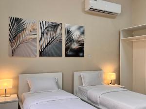 two beds in a room with three paintings on the wall at Pool Villa Saraya in Ras al Khaimah