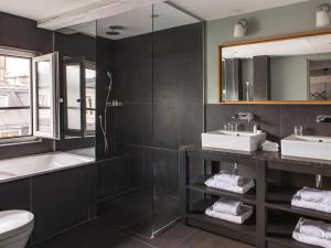 uma casa de banho com 2 lavatórios, uma banheira e um espelho. em New Hotel Roblin em Paris