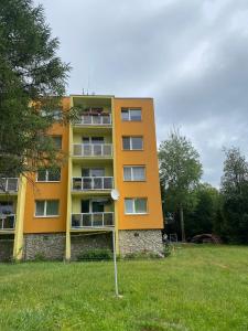 an orange building in a grassy field next to a building at Apartmán Hlboký potok in Vysoke Tatry - Tatranska Lomnica.