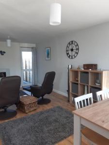 ein Wohnzimmer mit Stühlen, einem Tisch und einer Uhr in der Unterkunft The Getaway - Modern 2 Bedroom Brixham Bungalow with sea peeps in Brixham