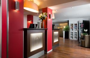 a lobby with red walls and a counter with flowers at Leonardo Hotel Frankfurt City Center in Frankfurt/Main