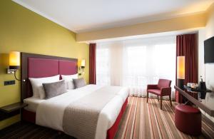 um quarto de hotel com uma cama grande e uma cadeira vermelha em Leonardo Hotel Berlin em Berlim