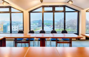 une salle de conférence avec des tables et des chaises et de grandes fenêtres dans l'établissement Leonardo Hotel Hamburg Elbbrücken, à Hambourg