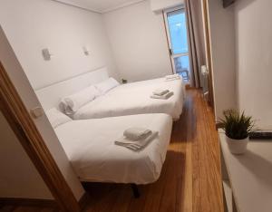 2 camas en una habitación con sábanas blancas y toallas en Pension Ipar, en Zarautz