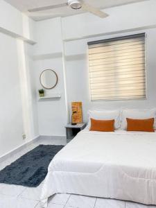 a white bedroom with a large white bed with orange pillows at The Nest - Cozy 3-Bedroom Condo with Pool in Shah Alam