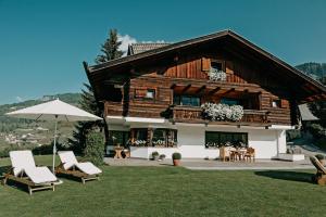 a large wooden house with chairs and an umbrella at Mountain Chalet Pra Ronch in Selva di Val Gardena