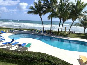 una piscina con sillas, palmeras y el océano en The Victorian Luxury Condo O-1, en Cabarete