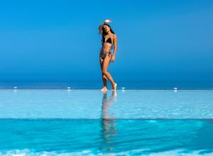 Atermono Boutique Resort & Spa في بلاتانيز: امرأة تمشي في الماء على الشاطئ