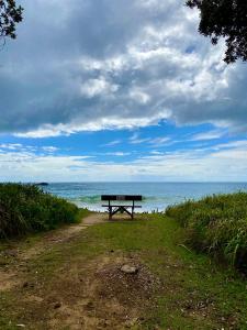 un banco sentado en un camino de tierra cerca del océano en Beachfront Retreat - Ducted Air - Free Wifi en Coffs Harbour