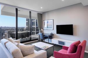 sala de estar con TV, sofá y sillas en Meriton Suites Kent Street, Sydney, en Sídney