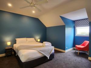 a blue bedroom with a bed and a red chair at Lady Heleena's At Strahan in Strahan