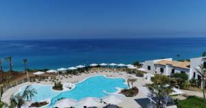 eine Luftansicht auf einen Pool mit Sonnenschirmen und das Meer in der Unterkunft Borgo Donna Canfora in Capo Vaticano