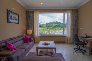 een woonkamer met een bank, een bureau en een raam bij Neugal Riverfront Resort in Pālampur