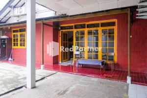 a red building with yellow doors and a bench outside at Ninja Room Pasteur Mitra RedDoorz in Bandung
