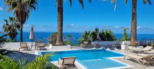 een zwembad met palmbomen en stoelen en de oceaan bij Maresía Village in Los Realejos