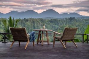 a table and two chairs on a deck with mountains in the background at Buahan, a Banyan Tree Escape in Payangan