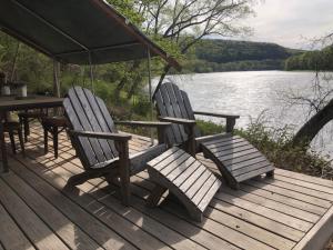 two chairs and a table on a wooden deck next to a lake at Tentrr Signature Site - River's Edge Sunset in Pond Eddy