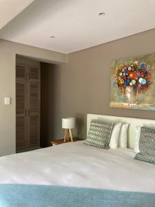 a bedroom with a white bed with a painting on the wall at Bloemenzee Boutique B&B in Gordonʼs Bay