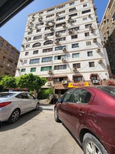 twee auto's geparkeerd voor een hoog gebouw bij Unique Apartment in Sheraton Heliopolis in Caïro