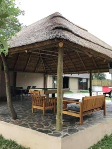 a pavilion with two benches and a table with a straw roof at LEHAE BNB in Mbabat