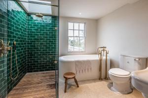 a bathroom with a tub and a toilet and green tiles at The Limes Benhall - Air Manage Suffolk in Saxmundham