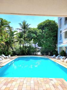 einen großen blauen Pool mit Stühlen und Bäumen in der Unterkunft Apartamento na Praia in Guarujá